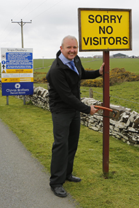 Scapa Distillery Manager Brian Macaulay removes the "No Visitors" sign at the distillery entrance following the opening of Scapa's new visitor center. Photo courtesy Chivas Brothers.